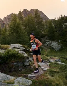 Atleta in corsa su un sentiero tra rocce e larici
